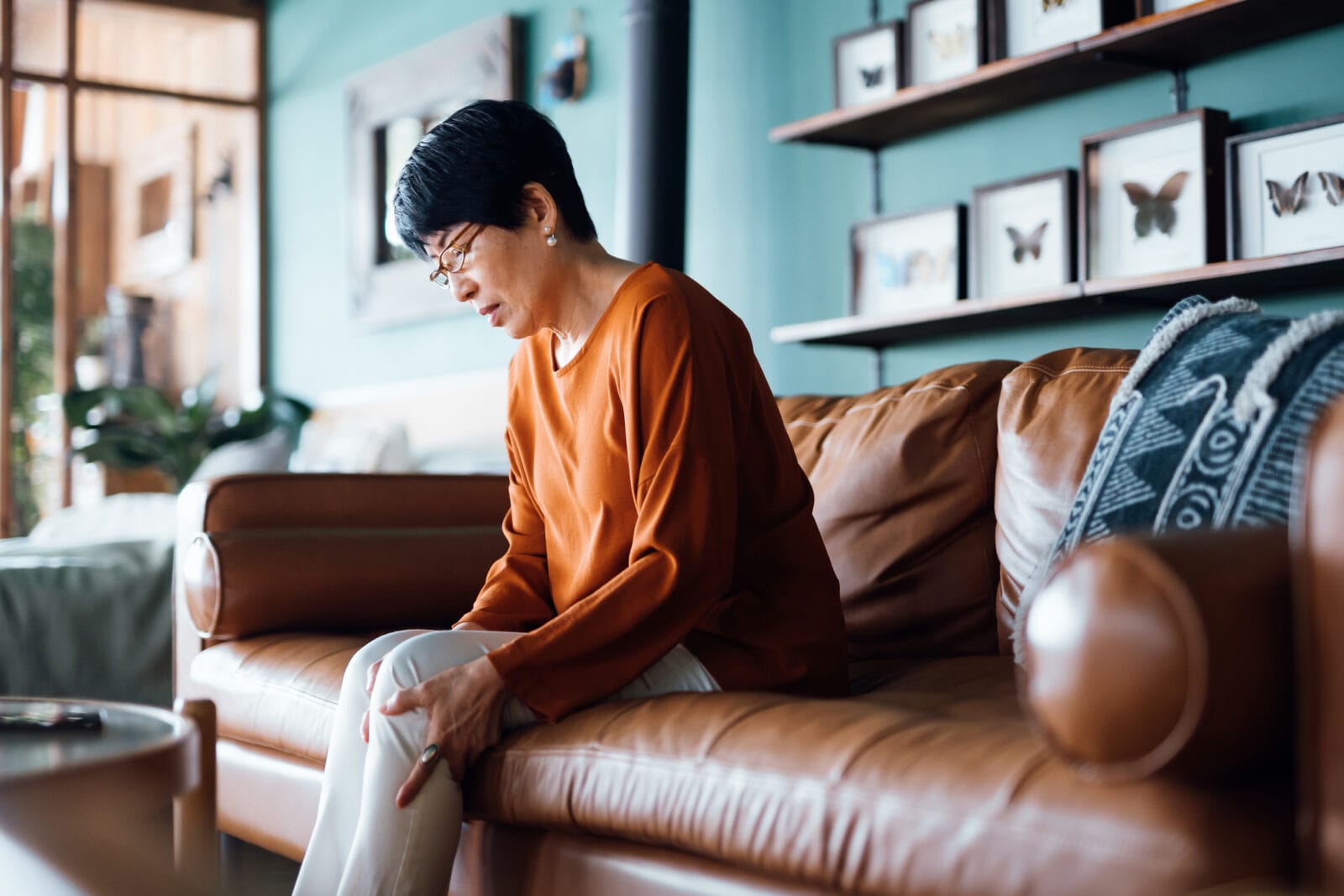 A woman holds her leg in pain while sitting on the sofa.