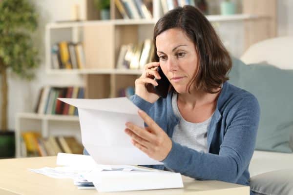 A woman sitting at a table, looking at papers and talking on the phone.