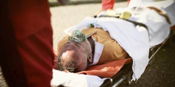 An elderly man on a stretcher with an oxygen mask.