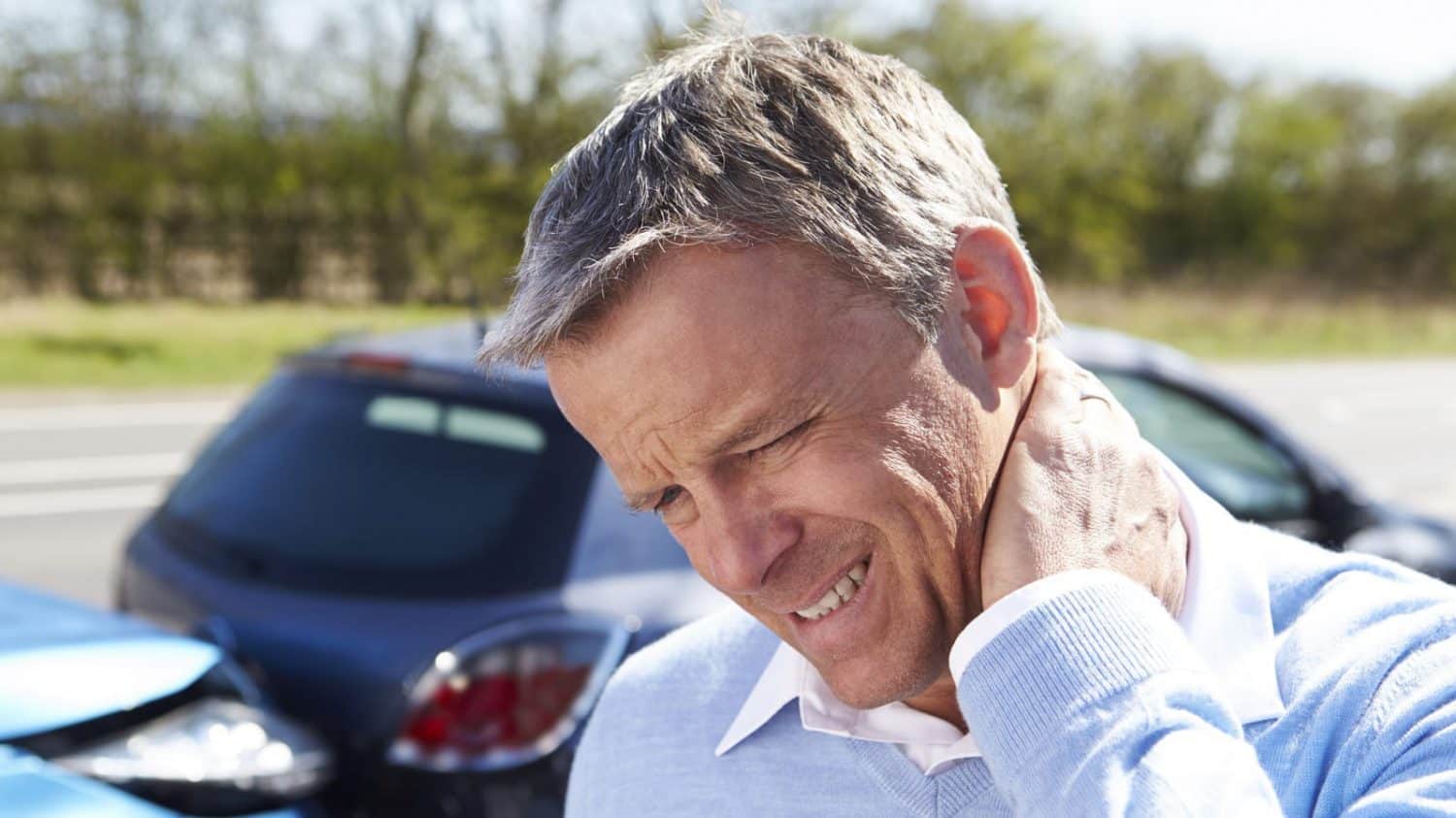 A man holding his neck after a car accident, indicating whiplash.