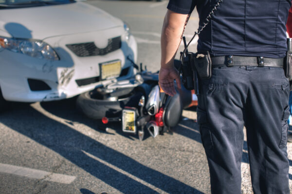 A police officer observes a slightly damaged vehicle that has collided with a motorcycle.