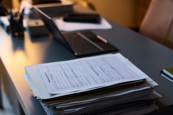 stack of documents on a lawyer's desk. A laptop, some pens, and other various office materials can also be seen on the desk.